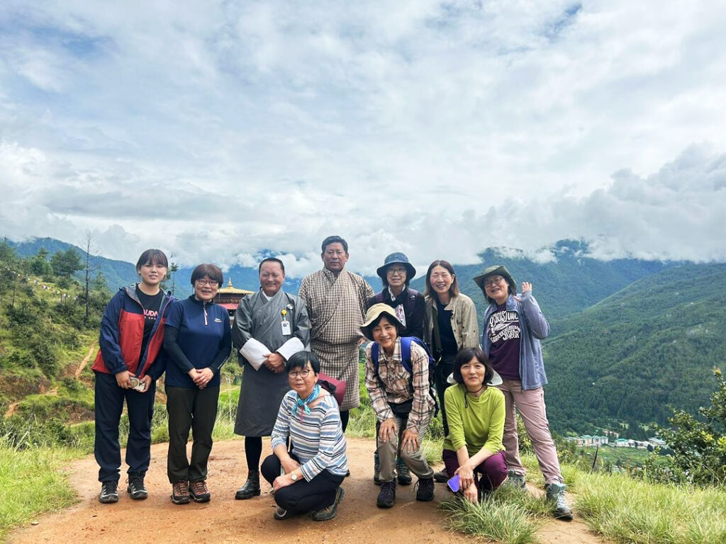 Group of trekkers posing together on a hilltop viewpoint overlooking forested mountains in Bhutan
