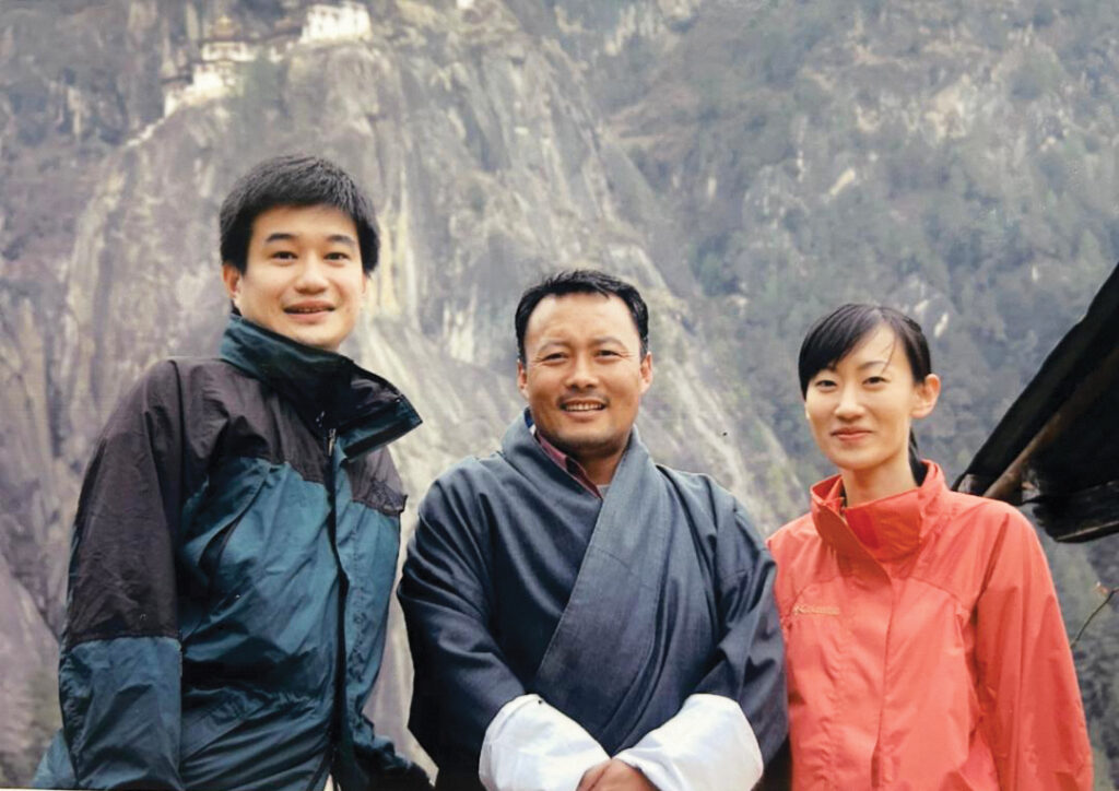 Travelers stand with a Bhutanese guide in traditional gho with Himalayan mountains behind them